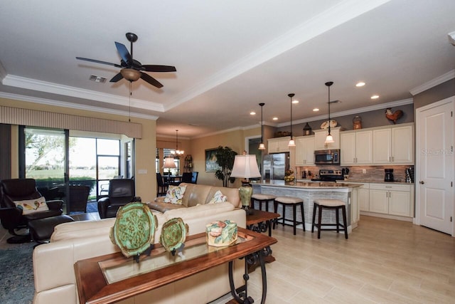 living room with a raised ceiling, crown molding, and ceiling fan with notable chandelier