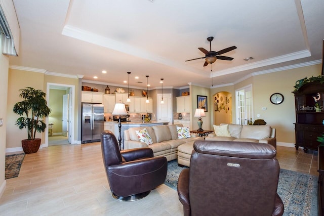 living room featuring a tray ceiling, ceiling fan, and ornamental molding