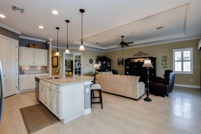 kitchen with pendant lighting, a kitchen island with sink, white cabinets, sink, and light stone countertops