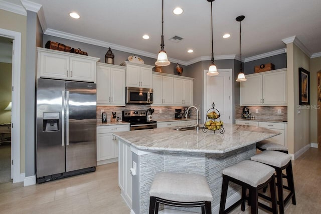 kitchen featuring white cabinetry, sink, stainless steel appliances, light stone counters, and an island with sink