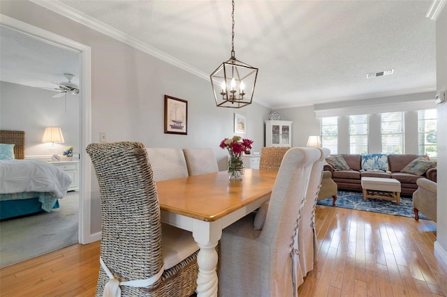 dining room with ceiling fan with notable chandelier, ornamental molding, a textured ceiling, and light wood-type flooring