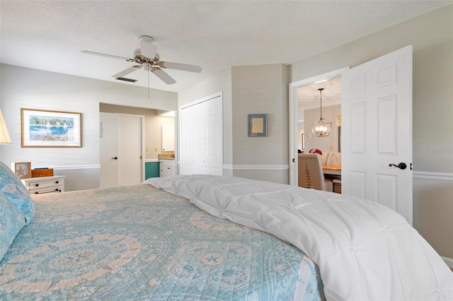 bedroom with ceiling fan with notable chandelier, a textured ceiling, and a closet