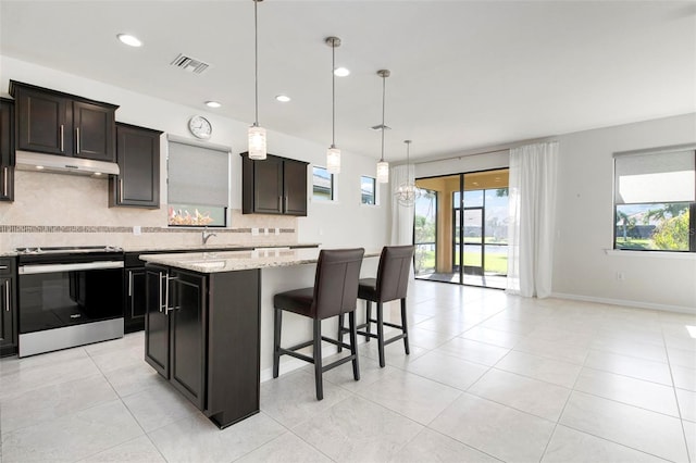 kitchen with pendant lighting, a center island, stainless steel electric stove, light stone countertops, and tasteful backsplash