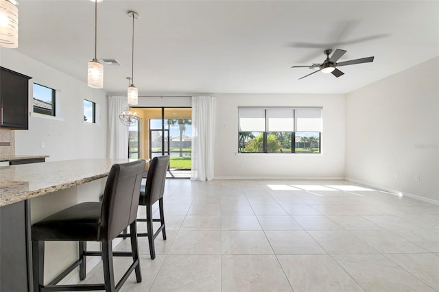 kitchen with pendant lighting, ceiling fan with notable chandelier, light stone countertops, light tile patterned floors, and a breakfast bar area