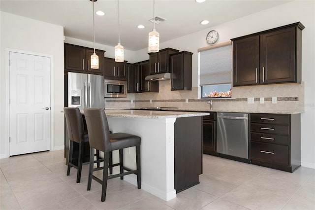 kitchen with light stone countertops, appliances with stainless steel finishes, decorative light fixtures, a kitchen island, and dark brown cabinetry