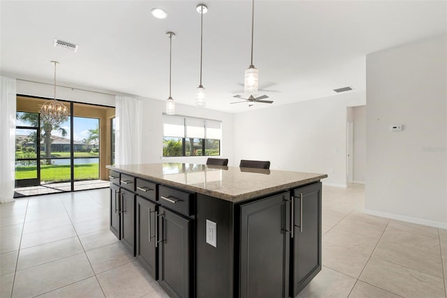 kitchen featuring light stone countertops, a center island, pendant lighting, light tile patterned flooring, and ceiling fan with notable chandelier