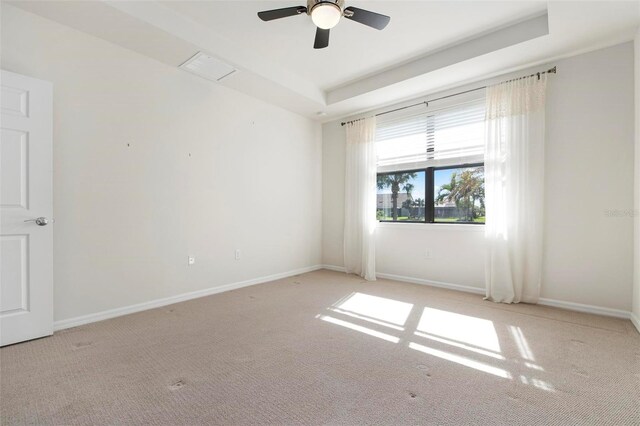 empty room with light carpet, a tray ceiling, and ceiling fan