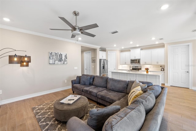 living room featuring ceiling fan, light hardwood / wood-style flooring, sink, and ornamental molding