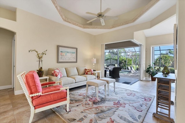 tiled living room with a tray ceiling and ceiling fan