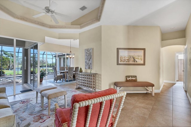 living room with ceiling fan with notable chandelier, a raised ceiling, and light tile patterned floors