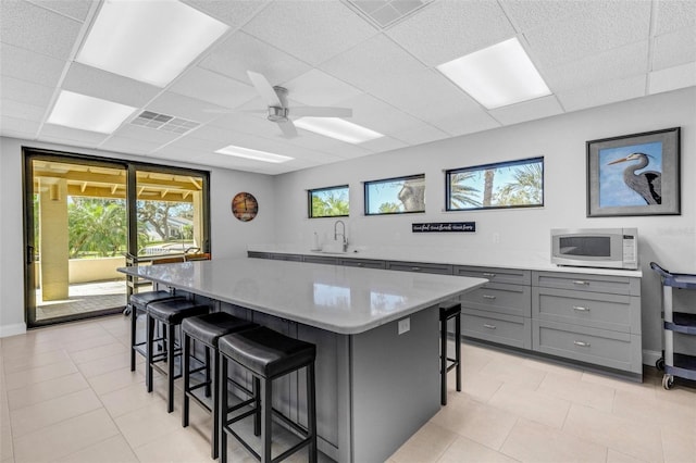 kitchen with a drop ceiling, stainless steel microwave, a kitchen breakfast bar, sink, and a kitchen island