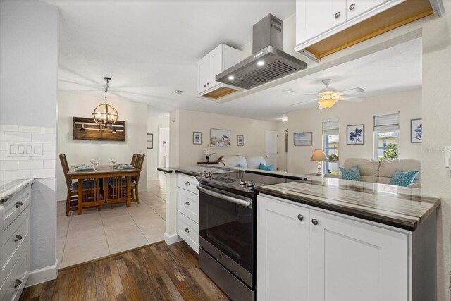 kitchen featuring ceiling fan with notable chandelier, dark wood-type flooring, wall chimney range hood, white cabinetry, and stainless steel electric range