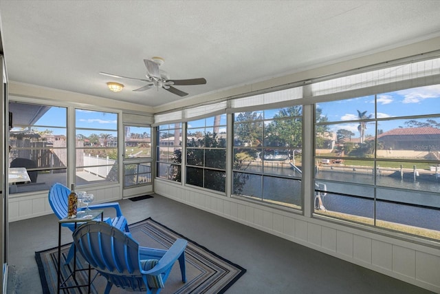 sunroom with ceiling fan and a water view