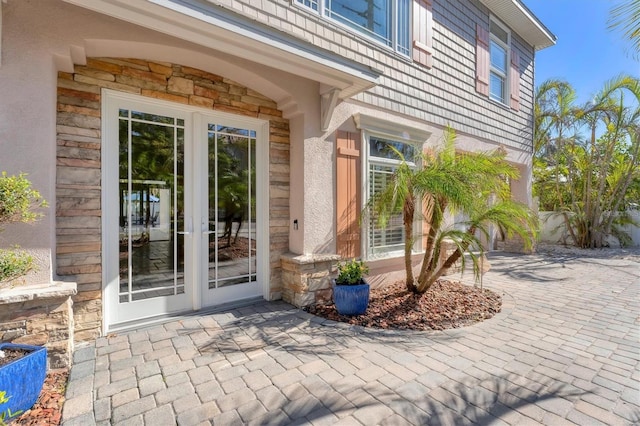 view of exterior entry with a patio area, stone siding, and stucco siding