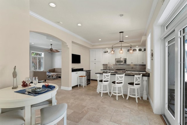 kitchen featuring white cabinets, crown molding, ceiling fan, tasteful backsplash, and a breakfast bar area