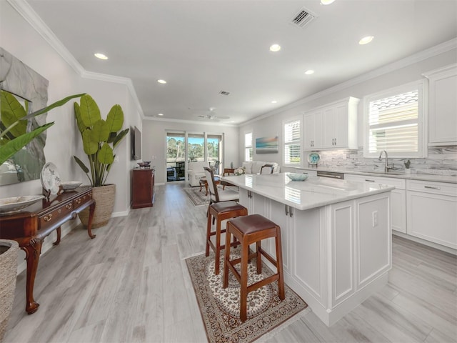 kitchen featuring ceiling fan, a kitchen island, light stone counters, light hardwood / wood-style floors, and white cabinets