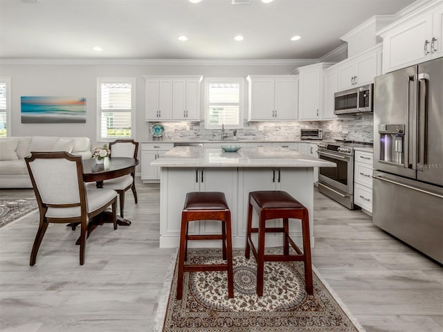 kitchen with white cabinetry, a center island, ornamental molding, and appliances with stainless steel finishes