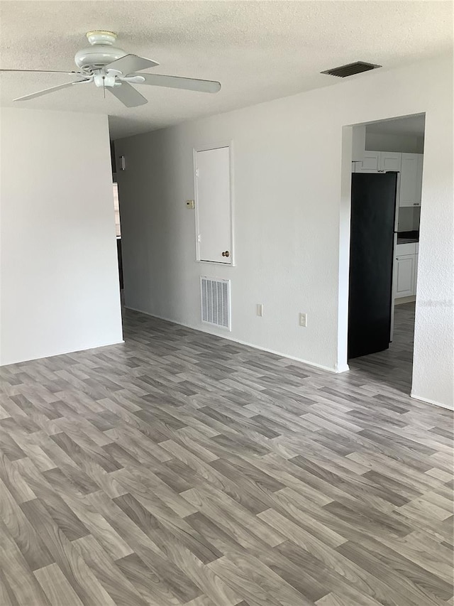 empty room with ceiling fan, light hardwood / wood-style flooring, and a textured ceiling