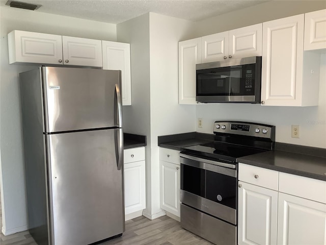 kitchen with white cabinets, a textured ceiling, stainless steel appliances, and light hardwood / wood-style flooring