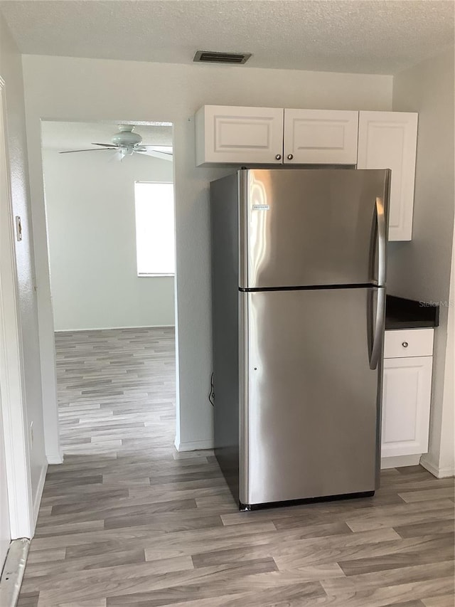 kitchen featuring stainless steel refrigerator, white cabinetry, ceiling fan, and light hardwood / wood-style floors