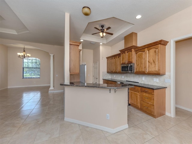 kitchen with crown molding, a tray ceiling, decorative backsplash, ceiling fan with notable chandelier, and appliances with stainless steel finishes