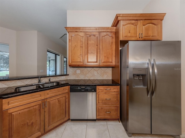 kitchen featuring sink, light tile patterned floors, stainless steel appliances, and dark stone counters