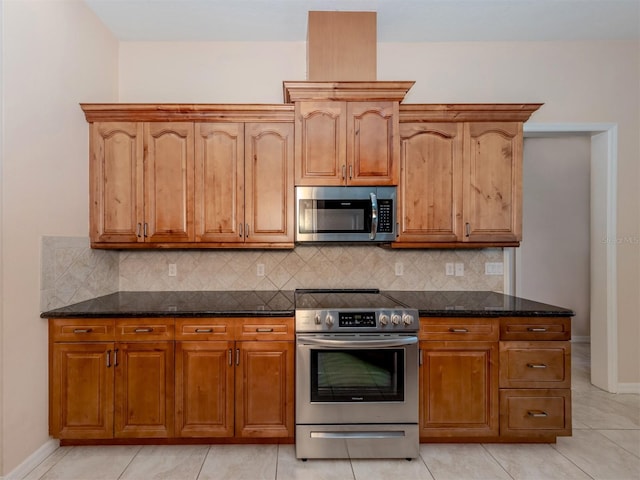 kitchen featuring decorative backsplash, light tile patterned floors, dark stone counters, and appliances with stainless steel finishes