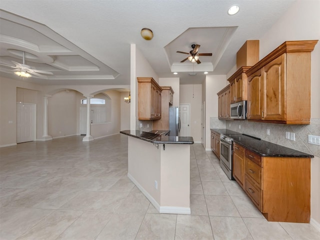 kitchen featuring a raised ceiling, backsplash, dark stone counters, and stainless steel appliances