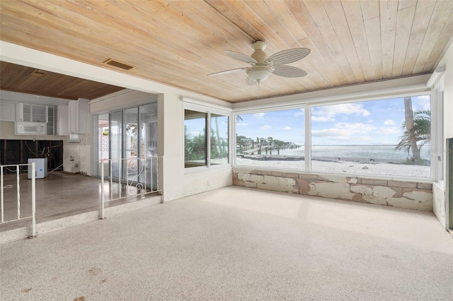 unfurnished sunroom with ceiling fan, a water view, wood ceiling, and a beach view