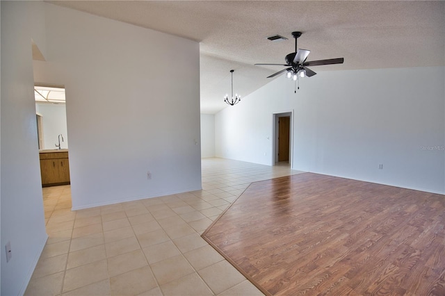 spare room with vaulted ceiling, light hardwood / wood-style flooring, a textured ceiling, and ceiling fan with notable chandelier