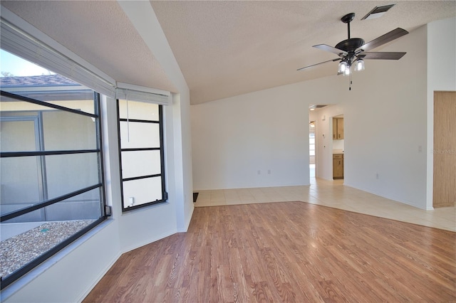 spare room with a textured ceiling, light hardwood / wood-style flooring, ceiling fan, and lofted ceiling