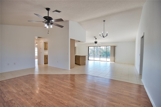 unfurnished room featuring ceiling fan with notable chandelier, a textured ceiling, high vaulted ceiling, and light hardwood / wood-style flooring