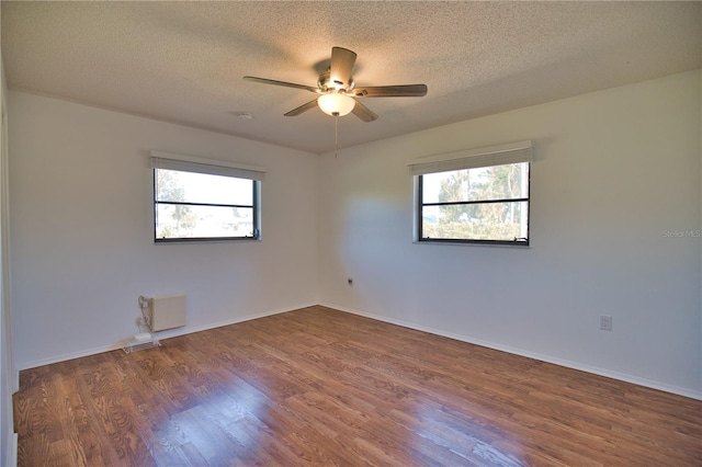 empty room with a textured ceiling, dark hardwood / wood-style flooring, a wealth of natural light, and ceiling fan