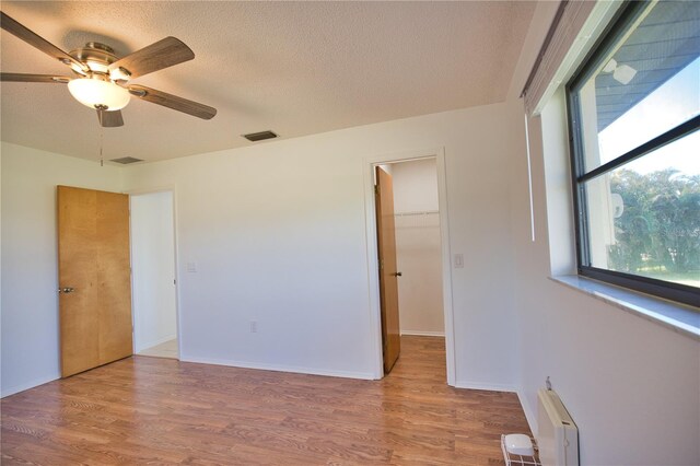 unfurnished bedroom featuring hardwood / wood-style floors, ceiling fan, and a walk in closet