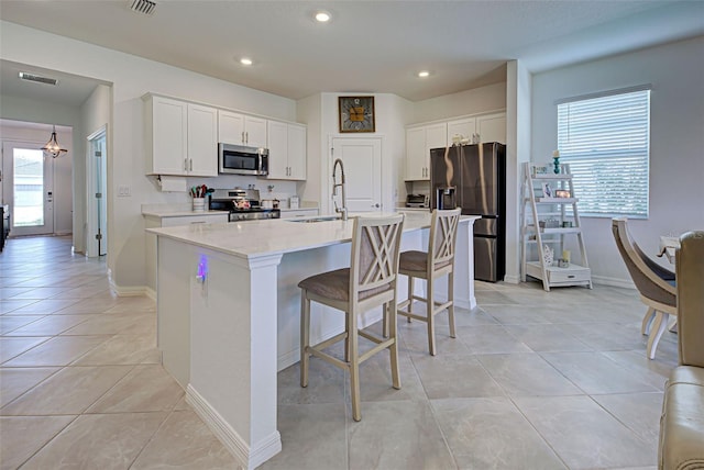 kitchen with a center island with sink, sink, appliances with stainless steel finishes, light tile patterned flooring, and white cabinetry