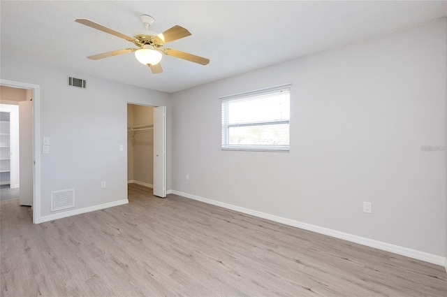 unfurnished bedroom featuring a walk in closet, ceiling fan, light wood-type flooring, a textured ceiling, and a closet