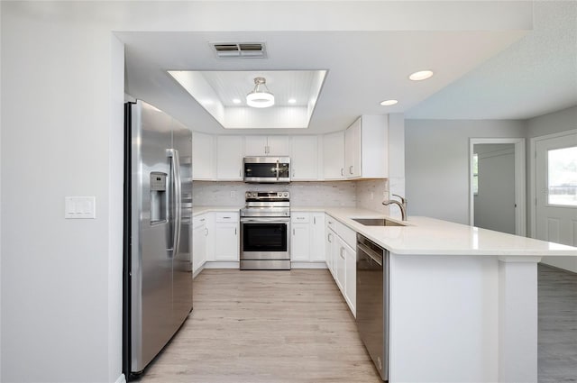 kitchen with kitchen peninsula, sink, light wood-type flooring, appliances with stainless steel finishes, and white cabinetry