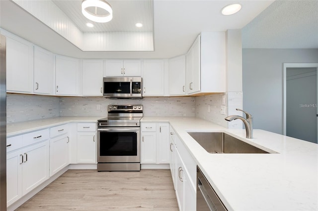 kitchen featuring decorative backsplash, appliances with stainless steel finishes, sink, light hardwood / wood-style flooring, and white cabinetry