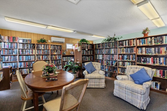 living area with a textured ceiling, wood walls, dark carpet, and a wall mounted air conditioner