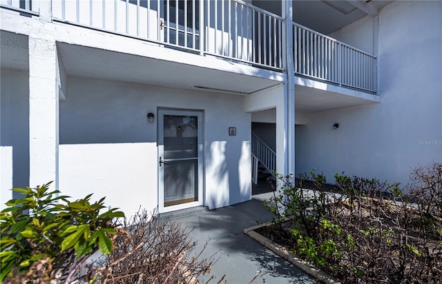 entrance to property featuring board and batten siding, a balcony, and stucco siding