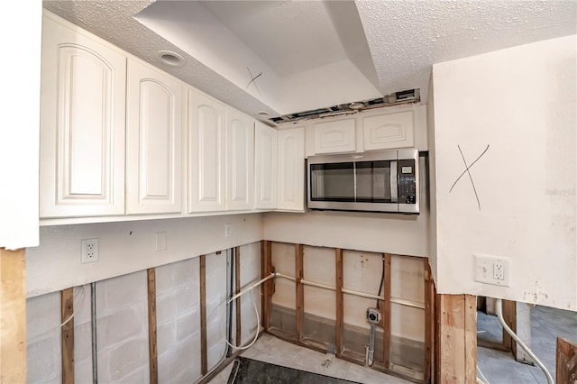 kitchen featuring stainless steel microwave, a textured ceiling, and white cabinetry