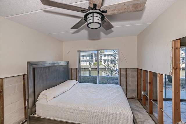 bedroom featuring a ceiling fan, access to outside, a water view, and a textured ceiling