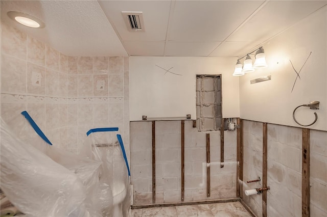 bathroom with a wainscoted wall, visible vents, and tile walls