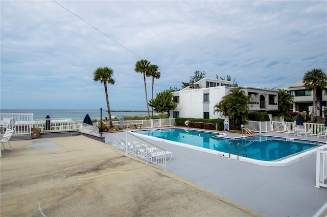 pool featuring a water view, fence, and a patio