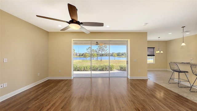 spare room featuring wood-type flooring, ceiling fan with notable chandelier, and a water view