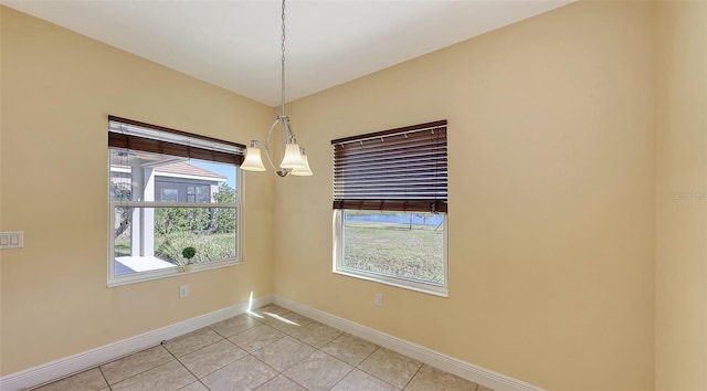 tiled spare room with a healthy amount of sunlight and a chandelier