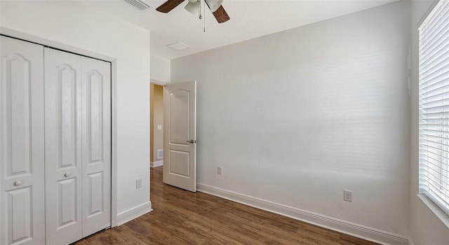 unfurnished bedroom with a closet, multiple windows, dark wood-type flooring, and ceiling fan