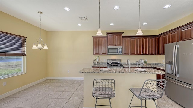 kitchen featuring a kitchen bar, a kitchen island with sink, decorative light fixtures, and appliances with stainless steel finishes