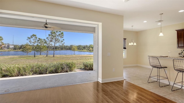 interior space with ceiling fan with notable chandelier, a water view, and light hardwood / wood-style floors