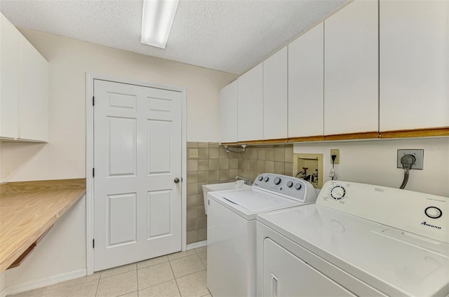 clothes washing area featuring light tile patterned floors, cabinets, a textured ceiling, and independent washer and dryer